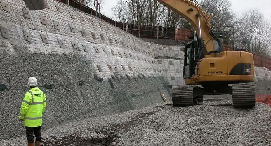 نیلینگ به طور کلی روش استفاده از نیلینگ به این صورت است که ابتدا دیوار ها رگلاژ می شوند و سپس شبکه ای از مش های فولادی به وسیله میخ های به طول ۵۰ سانتی متر به درون آنها رانده می شود و روی سطح با سیمانی به قطر ۱۰ تا ۱۵ سانتی متر پوشیده خواهد شد مرحله بعدی گمانه و جا زدن میلگرد ها است در ادامه این روش دوغاب سیمان به محل تزریق می شود و پس از انجام این مرحله هد نیل ها بسته خواهد شد در واقع یکی از بهترین روش ها برای مقابله با زلزله و مستحکام سازی دیوارهای باربر با اجرای روش نیلینگ امکان پذیر می باشد. در این حالت نیروی رانش خاک ناشی از زلزله و لغزش ها به هدنیل ها از طریق توده خاک اعمال می شود نیروی رانش خاک از طریق سیستم نیلینگ مهار می شود و به سطح ساختمان و دیوارها منتقل نمی شود این روش به دلیل بهبود و استحکام ساختمان ها بعدها توسط مهندسان فرانسوی و آلمانی در پایدار سازی تونلها و کوله پله ها استفاده شد نیلینگ سازه نگهبان محسوب می شود و باعث افزایش قدرت اسکلت بندی ساختمان می شود. نیلینگ یا میخ کوبی چیست نیلینگ یکی از محبوب ترین روش های حفاظت جداره و دیواره است و سرعت بالایی در اجرای آن وجود دارد زیرا چند بخش کار آن را می توان به شکل همزمان انجام داد. پایدارسازی دیواره با روش نیلینگ در طیف گسترده ای از انواع خاک ها قابل پیاده سازی است و این امکان وجود دارد که در گود قائم نیز اجرا شود. در گودبرداری هایی که عمق گود بسیار زیاد است و نمی توان از راه گود برداری مایل و یا پله ای استفاده کرد، از شیوه نیلینگ یا میخ کوبی خاک برای انجام این کار استفاده می کنند. این روش کاربرد های زیادی در پایدار کردن شیب ها و شیروانی ها و افزایش ظرفیت حمل بار آن ها و ایجاد محدودیت در تغییر شکل مخصوصا در پروژه های شهری است. برای این که بتوان از این روش جهت پایداری سازه استفاده کرد، باید خاک محل تا حد اقل تا عمق ۱.۵ متری توان حفظ پایداری را داشته باشد. بعد از این که خاک برداری پله اول انجام شد، نخستین ردیف میخ ها اجرا می شوند و پس از آن یک رویه بتنی روی کار کشیده می شود. پس از آن نیز همین روند تا زمانی که به تراز آخر گود برداری برسید باید ادامه پیدا کند. به کار بردن این روش برای پایدار سازی سازه هایی که در زیر زمین احداث می شوند، مانند ایستگاه های مترو بسیار رایج و مناسب است. نقاط قوت و نقاط ضعف پایدارسازی جداره به روش نیلینگ روش نیلینگ تنها یکی از روش های پایدارسازی دیواره و گودال است که مزایا و معایب خود را دارد. شرکت ترانشه ارائه دهنده خدمات آزمایش خاک و مکانیک خاک می باشد. در صورت نیاز به اطلاعات بیشتر با ما تماس بگیرید. نیلینگ نقاط قوت روش نیلینگ از این روش می توان برای مکان هایی استفاده نمود که فضاها بسیار نزدیک به هم هستند و بناهای زیادی در نزدیکی محل پروژه احداث شده اند. به همین دلیل روشی بسیار مناسب برای فضاهای شهری است. آزمایش تک محوری روش نیلینگ یک روش بسیار سازگار با محیط زیست است و از این جهت دغدغه بسیاری از افراد را رفع می کند. این روش پایدارسازی انعطاف زیادی در اجرا دارد. منظور از اجرا امکان سازگاری سازه با ناهمواری ها و وضعیت های مختلف زمین است. این سازه ها برای اجرا شدن در نزدیکی سازه هایی که حساس هستند و امکان نشست در آن ها وجود دارد گزینه های بسیار خوبی هستند. نیلینگ یک روش مقرون به صرفه است. مصالح و ابزاری که در روش نیلینگ به کار می روند باعث می شوند که قیمت نهایی سازه بسیار کم تر از انواع دیگر روش های پایدار سازی باشد. برای سازه هایی که کم تر از ۱۸ ماه زمان برای ساخته شدن نیاز داشته باشند و همچنین سازه هایی که به زمانی طولانی تر نیاز دارند قابل استفاده است زیرا نیلینگ به شکل های موقت و دائم قابل اجرا است. در موقعیت هایی که به دلیل محدودیت فضا باید از ابزار و وسایل کوچک تری استفاده شود، به کار بردن روش نیلینگ توصیه می شود. شرکت ترانشه ارائه دهنده خدمات طراحی ساختمان و سازه نگهبان می باشد. در صورت نیاز به خدمات دهی با ما تماس بگیرید. نقاط ضعف روش نیلینگ این روش با کمک گرفتن از بناهای اطراف قابل انجام است به همین دلیل باید از صاحبان ساختمان های اطراف برای به کار گرفتن این روش رضایت جلب شود. ابزاری که برای اجرای نیلینگ به کار گرفته می شوند صداهای زیادی تولید می کنند و ممکن است که موجب آزردگی سکنه محل شود. پایدار سازی گود و دیواره به روش نیلینگ جداره هایی که میخ کوبی شده اند می توانند به دو شکل موقت یا دائمی پیاده سازی شوند. میخ کوبی موقت: میخ کوبی هایی که به شکل موقت انجام می شوند، طول عمری کم تر از هجده ماه دارند. گاهی اوقات دیده می شود که یک ترانشه یا گودال به شکل موقت میخ کوبی شده است اما ساختن آن بیش تر از هجده ماه طول کشیده است. در این صورت باید از سیستم های گود برداری دائمی برای تثبیت استفاده شود. برای این کار در زمین گودال هایی حفر می کنند که نیل ها یا میلگرد ها درون آن ها قرار می گیرد و فضای خالی با دوغاب سیمان پر می شود. میخ کوبی دائم: هنگامی که سازه ای به شکل دائم میخ کوبی شده باشد، طول عمر آن ها بیش از ۱۸ ماه طول خواهد کشید. شرکت ترانشه خدمات دهی در زمینه نشست ساختمان و بهسازی خاک را دارد. در صورت نیاز به خدمات دهی با ما تماس بگیرید. نیلینگ نیلینگ در چه پروژه هایی کاربرد دارد؟ با روش نیلینگ ترانشه هایی که برای ساختن بزرگ ها و راه آهن ها احداث می شوند، پایدار می شوند. در ساختن سازه های زیر زمینی و دیواره تونل های زیر زمینی نقش مهمی دارد و سبب پایداری و امنیت آن ها می شود. در سازه های مختلفی که در شهر ها ساخته می شوند، قسمت های زیادی مانند سازه های اطراف گود و ایستگاه های مترو زیر زمینی حفاظت می شوند. در زمین هایی که دارای خاک های سست هستند که امکان ریزش را افزایش می دهند می توان با روش نیلینگ استحکام را افزایش داد. نیلینگ یا میخ کوبی به چه شکلی قابل انجام است؟ در ابتدا گود برداری انجام می شود و برای گود ها پله بعدی عملیات نیز حفر می شود. خاک برداری باید قدم به قدم انجام شود و در هر مرحله میخ کوبی آن انجام شود و سپس خاک برداری مرحله بعدی شروع شود. سپس چال هایی برای قرار دادن مهار کششی نیل ها یا میلگرد ها حفر می شوند. این چال ها باید در فاصله های متناسب و مشخصی حفر شوند. آرماتورها که معمولا قطری بین ۱۸ تا ۴۰ میل دارند، داخل چال هایی که حفر شده اند قرار می گیرند و معمولا فضا با دوغاب سیمان پر می شود. دوغاب مورد استفاده معمولا از آب و سیمان ساخته می شود و در برخی موارد ماسه و مواد شیمیایی دیگری نیز به آن می افزایند. سیستم زهکشی و شاتکریت جداری اجرا می شود و ضخامت فولادی نصب می شود. در نهایت پس از آخرین مرحله حفاری شاتکریت اجرا می شود. شاتکریت به معنای ریختن بتن برای پیشگیری از فرسایش سازه است. درز انقطاع و نحوه محاسبه و نکات اجرایی آن روش های ایجاد نیلینگ به چه صورت می باشد اغلب طرح های عمرانی برای استحکام سازی به نیلینگ نیاز دارند ترانشه های راه آهن و بزرگراه ها، ساخت سازه های نگهبانی گود برداری شده جهت احداث ساختمان های بلند و چند طبقه و تثبیت زمین هایی که دارای شیب هستند از جمله مهم ترین مواردی هستند که باید دارای نیلینگ و دیوار های باربر مستحکم باشند نیلینگ دیوارها به معنای تسلیح برجای خاک موجود در زمان نصب می باشد. به طور خلاصه در این روش میلگرد های نزدیک به هم در یک سطح شیب دار ملایم در حدود ۱۰ تا ۲۰ درجه در کنار یکدیگر در محل اجرای سازه قرار می گیرند اصول اولیه نیلینگ بر پایدارسازی گوه لغزش ها به وسیله نیل های استوار است. اثر مسلح سازی برای بهبود پایداری میله ها با دو روش زیر حاصل می شود: افزایش نیروی قائم در زمین در نتیجه افزایش مقاومت برشی در خاکهای اصطحکاکی کاهش نیروی رانشی در اثر لغزش های ناشی از زلزله در خاک های بهم چسبیده پس از نصب میلگرد ها در سطح شیب دار زمین دیواره سطحی کم ضخامت که شامل شاکریت ها یا تسلیحات سبک می شود با استفاده از مسالح مقاوم مانند بتن پوشیده می شود ضخامت هر کدام از شاکریت ها در حدود ۱۰ تا ۱۵ سانتی متر است و هدف اصلی از اجرای آنها جلوگیری از فرسایش سطحی خاک و ایجاد سطح مناسب برای سازه های احتمالی بعدی است. ایجاد سطح یکنواخت و یکپارچه باعث پخش یکنواخت نیرو در تمام سطح می شود در نتیجه احتمال ریزش ساختمان در اثر لغزش های احتمالی به صورت چشمگیری کاهش پیدا می کند همچنین افزایش بازدهی عملکرد خاک در بخش های نزدیک به گود و نواحی سست تا حدود زیادی قابل پیش بینی می باشد. در صورت نیاز به خدمات دهی در زمینه انکراژ و میکروپایل با مجموعه ترانشه تماس بگیرید. soil nailing نیلینگ روش های ایجاد نیلینگ تاکنون روش های اجرای نیلینگ گسترش زیادی یافته است این سازه نگهبان به دو صورت موقت و دائمی اجرا می شود میخکوبی های موقت بسته به نوع خاک و سازه دارای طول عمر بین یک سال تا ۱۸ ماه می باشند اما نیلینگ های دائمی عمری بیش از این حد دارند روش های مختلف پایدار سازی ترانشه باعث شده برای هر نوع از ساختمان ها از نیلینگ خاصی استفاده شود. روش پیشنهادی برای اکثر نیلینگ و انکراژ ها پایدار سازی دیوار گودها مشتمل بر ۵ مرحله اصلی گود برداری، مقطعی، حفاری گمانه ها، نصب میلنگ، تزریق دوغاب سیمان، بتن پاشی و نصب صفحات و پیچ و مهره های میلنگ ها می شود پس از انجام این مرحله گود برداری آغاز می شود. گودبردای تا جایی انجام می شود که دیواره های گود بتوانند در مدت بین ۱۲ تا ۴۸ ثبات خود را حفظ کنند خاکبرداری های نیلینگ باید مرحله به مرحله و با توجه به نوع سازه انجام شود. امروزه بیشتر عملیات فوق به وسیله دستگاه نیلینگ انجام می شود قیمت نیلینگ براساس نوع سازه نیلینگ ؛ دوام آن، نوع خاک و غیره قبل از شروع عملیات بررسی می شود. حفاری دستی و حفاری ماشینی توسط مجموعه ترانشه قابل انجام است. در صورت نیاز به خدمات دهی با ما تماس بگیرید. روش انجام نیلینگ مرغوب ساختمان و مطمئن و جلوگیری از ضربه اگر زمین ساختمان سازی در شیب قرار گیرد بهترین راه برای هموار کردن آن میخ کوبی خاک با استفاده از میله های فولادی است این روش یکی از روش های خلاقانه مهندسان استرالیایی برای هموار ساختن زمین های شیب دار است برای این کار باید ابتدا دیوارها رگلاژ شوند. سپس شبکه ای از مش های فولادی با میخ های ۵۰ سانتی متری نصب خواهند شد و روی آنها به ضخامت حدود ۱۰ تا ۱۵ سانتی متر بتن ریزی می شود این عمل به دلیل استفاده از بتن یک دست در زیر ساختمان باعث هموار شدن زمین و مقاوم سازی آن در برابر لرزش های احتمالی می شود. همچنین از زمین هایی بلا استفاده که در دره یا شیب کوه قرار دارند برای ساختمان سازی می توان استفاده کرد. آزمایش هم ارز ماسه نیلینگ و انکراژ برای استفاده از زمین هایی که در سطوح غیر مسطح قرار دارند و شیب زیادی دارند اهمیت زیادی دارد استفاده از این روش جلوی سیلاب های ناگهانی در دره ها را می گیرد و باعث جلوگیری از ضربه زدن به دیوار های ساختمان می شود مرحله پس از حفاری و بتن ریزی برای نیلینگ ساختمان ها گمانه ها و جا زدن میلگرد های فولادی است در ادامه گمانه ها باید دوغاب سیمان به محل تزریق شود و سپس نیل ها بسته شوند. عملا استفاده از این روش جلوی آسیب های رانش زمین را تا حدود بسیار زیادی می گیرد استفاده از مصالح قوی و سخت مانند سیمان در روش نیلینگ ساختمان مانع نفوذ آب به زیردیوارها و پایه های ساختمان ها می شود گاها از روش نیلینگ ساختمان برای افزایش قدرت پایه ریزی ساختمان های بلند حتی در زمین های هموار استفاده می شود. نیلینگ تنها برای ساختمان سازی استفاده نمی شود از این روش گاها برای طرح های عمرانی مختلف مانند تثبیت تراشه های خطوط راه آهن و بزرگراه ها استفاده می شود. همچنین ساخت سازی های گود برداری شده در مناطق شهری برای ساخت سازه های بسیار بلند و مرتفع که ممکن است گاها دارای چندین طبقه زیر زمین باشند باید برای پایه سازی های مستحکم از روش نیلینگ استفاده کنند. پارکینگ های طبقاتی با تعداد زیادی طبقه زیر زمین از انواع سازه های دارای فونداسیون نیلینگ می باشند. مجموعه ترانشه قادر به ارائه خدمات خرپا و انکراژ می باشد. در صورت نیاز به خدمات دهی با ما تماس بگیرید. روش انجام نیلینگ مرغوب ساختمان و مطمئن برای انجام نیلینگ ساختمان هر چقدر که لوله های فولادی به هم نزدیک تر باشند پایه ریزی نیلینگ قوی تر خواهد شد برای سطوحی با شیب ملایم بین ۱۰ تا ۲۰ درجه قائم بر سطح زمین معمولا در محل گود برداری شده از میخ هی فولادی استفاده می شود برای این کار میله های فولادی باید تحت تاثیر تنش های کششی قرار گیرد تا پایداری آنها برای فوندانسیون دیوار های باربر بررسی شود و از توانایی آنها اطمینان حاصل شود. هزینه نیلینگ ساختمان بسته به تعداد میله های فولادی و نوع آنها یا نسبت کار گذاری این میله ها در زمین دارد نیل ها برای پایداری سختمان در زمان لغزش استفاده می شوند. در روش نیلینگ فضای خالی در خاک به وسیله ذرات درشت به صورت گوه پر می شوند و با استفاده از میله های فولادی این گوه به حجم پشتی خاک دوخته خواهد شد و براین اساس گوه ها باعث پایداری می شوند این عملیات در واقع یک مقطع مسطح در خاک ایجاد می کند که نسبت به زلزله بسیار مقاوم می باشد و همچنین توانایی نگهداری خاک پشت را دارد. این مسطح سازی در خاک به صورت پسیو عمل می کند و به عنوان نیلینگ سازه نگهبان در سازه های عمرانی ایفای نقش دارد میخ های به کار رفته در نیلینگ و میخکوبی قالبا در کشش ها ایفای نقش می کنند ولی درشرایط خاصی در شرایط خمشی و برشی هم می توانند مقاومت کنند. آزمایش ژئوتکنیک توسط مجموعه ترانشه قابل انجام است. در صورت نیاز به اطلاعات بیشتر با ما تماس بگیرید. اثر مسلح سازی زمین با روش نیلینگ به دو صورت ایفای نقش می کند ایجاد نیروی قائم و مستحکم و در نتیجه ایجاد مقاومت برشی در خاک در زمان زمین لرزه کاهش نیروهای رانشی زمین در حالات اصطحکاکی در خاک پس از نصب میلگرد های فولادی در زمین یک دیواره سطحی با ضخامت بسیار کم با تصلیحات سبک سطح گود برداری شده را می پوشاند ضخامت این دیواره شاکریت باید در حدود ۱۰ تا ۱۵ سانتی متر باشد هدف اصلی از ایجاد این دیواره کم ضخامت با استفاده از مصالح نسبتا سبک جلوگیری از فرسایش سطحی خاک زیرین ساختمان است و نشت خاک می باشد. کلام آخر برای دریافت مشوره و یا نیزا به خدمات نیلینگ یا میخکوبی با شرکت ترانشه در تماس باشید. نیلینگ چیست؟ نیلینگ به دلیل استحکام بالا و سرعت بالا در اجرا، یکی از بهترین روش ها برای حفظ جداره و دیوار می باشد. نقاط قوت استفاده از نیلینگ چیست؟
